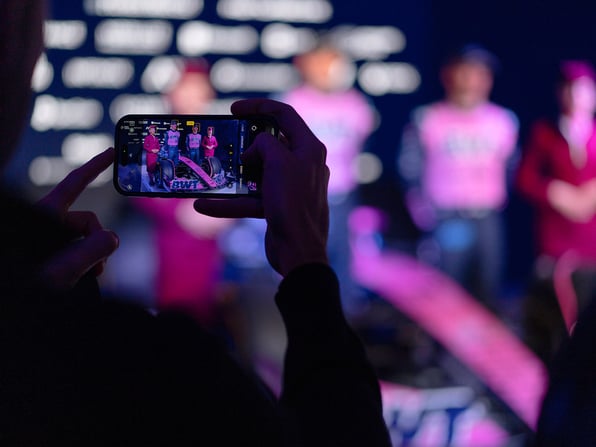 Someone holding a phone up to take a photo, and on the phone screen is a photo of BWT Alpine F1 team drivers at a launch event