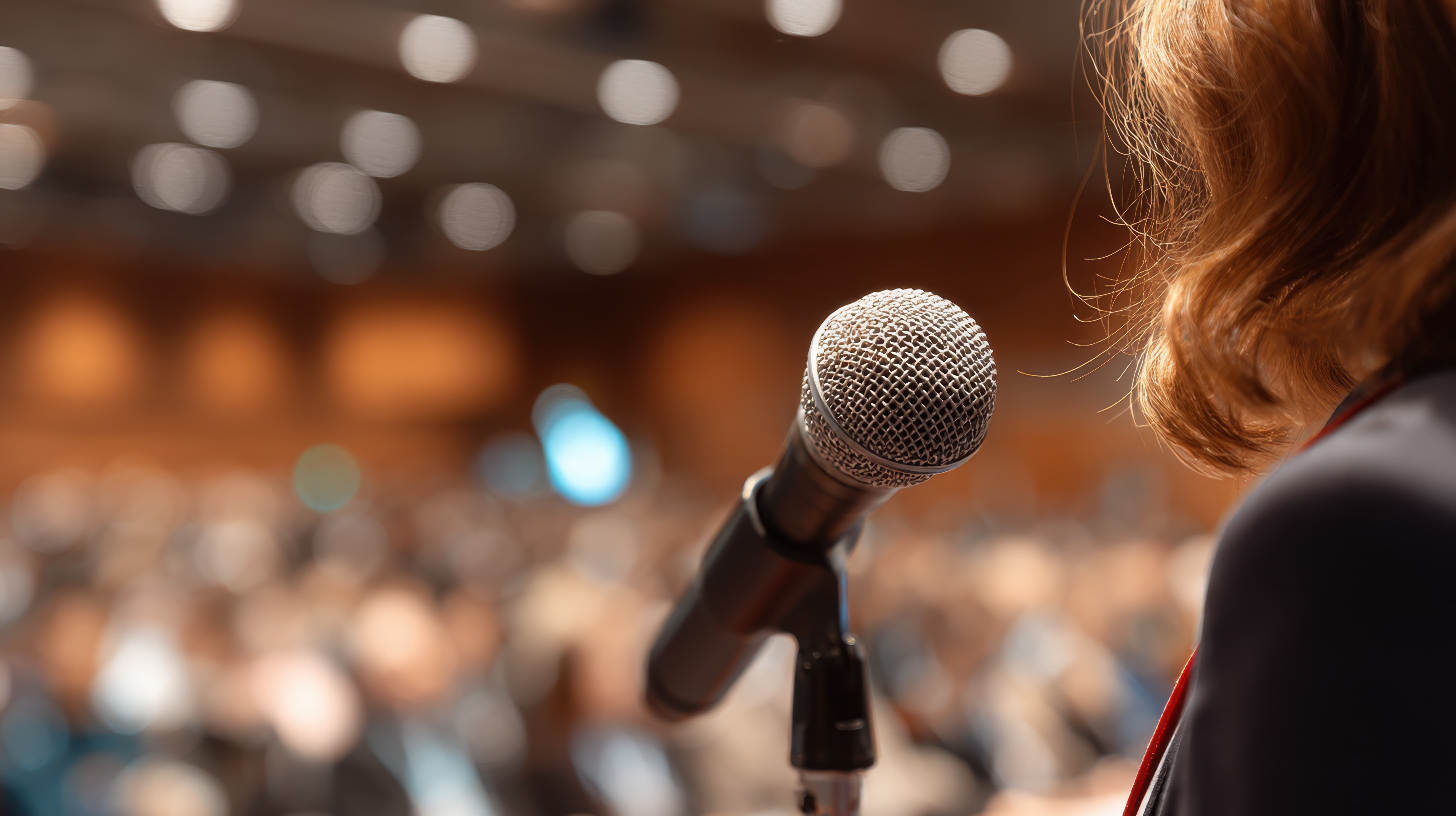 A woman speaking into a microphone in front of a corporate audience