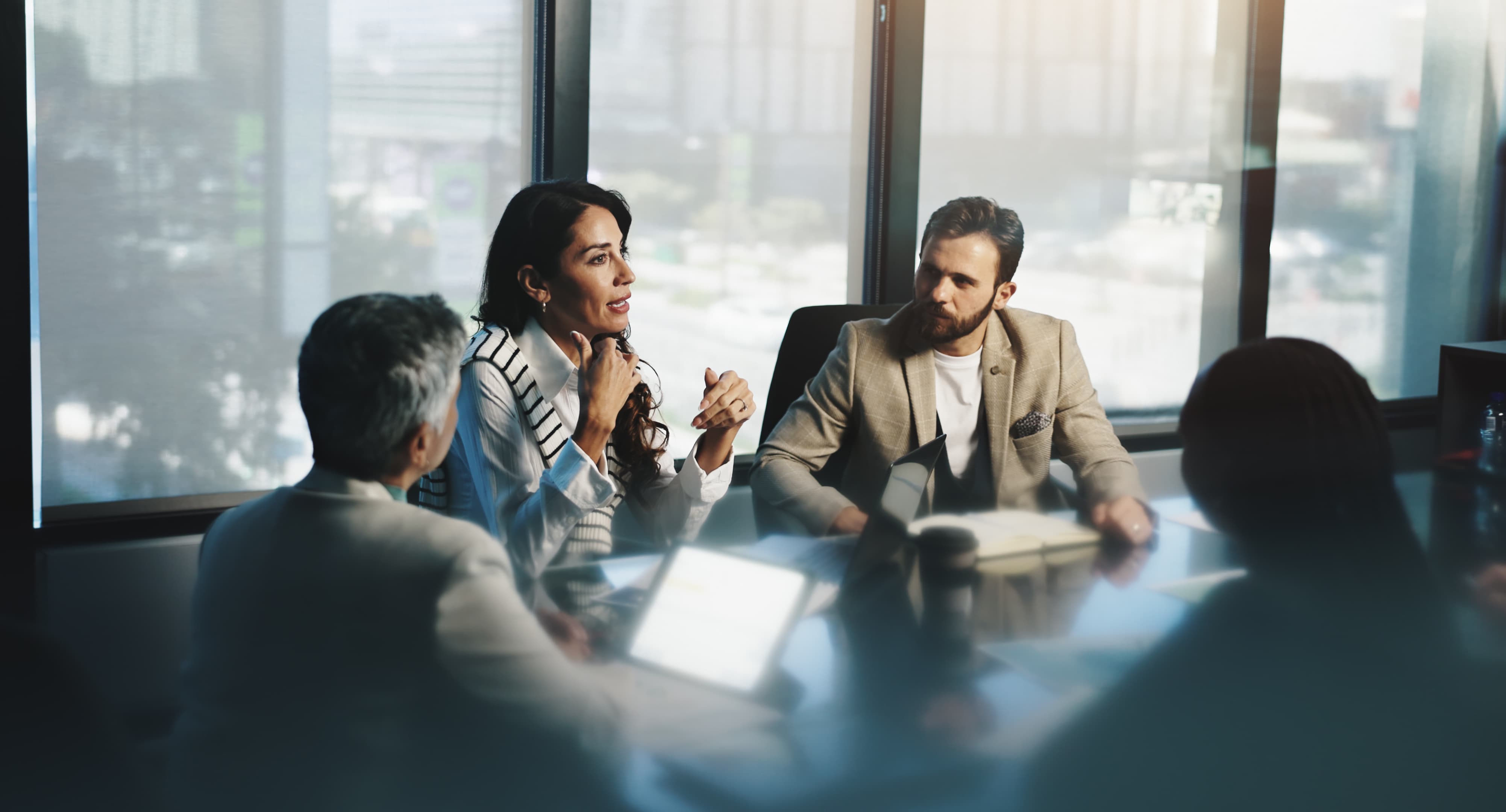 A workplace meeting where a woman is speaking to two male colleagues, one of whom has a laptop open