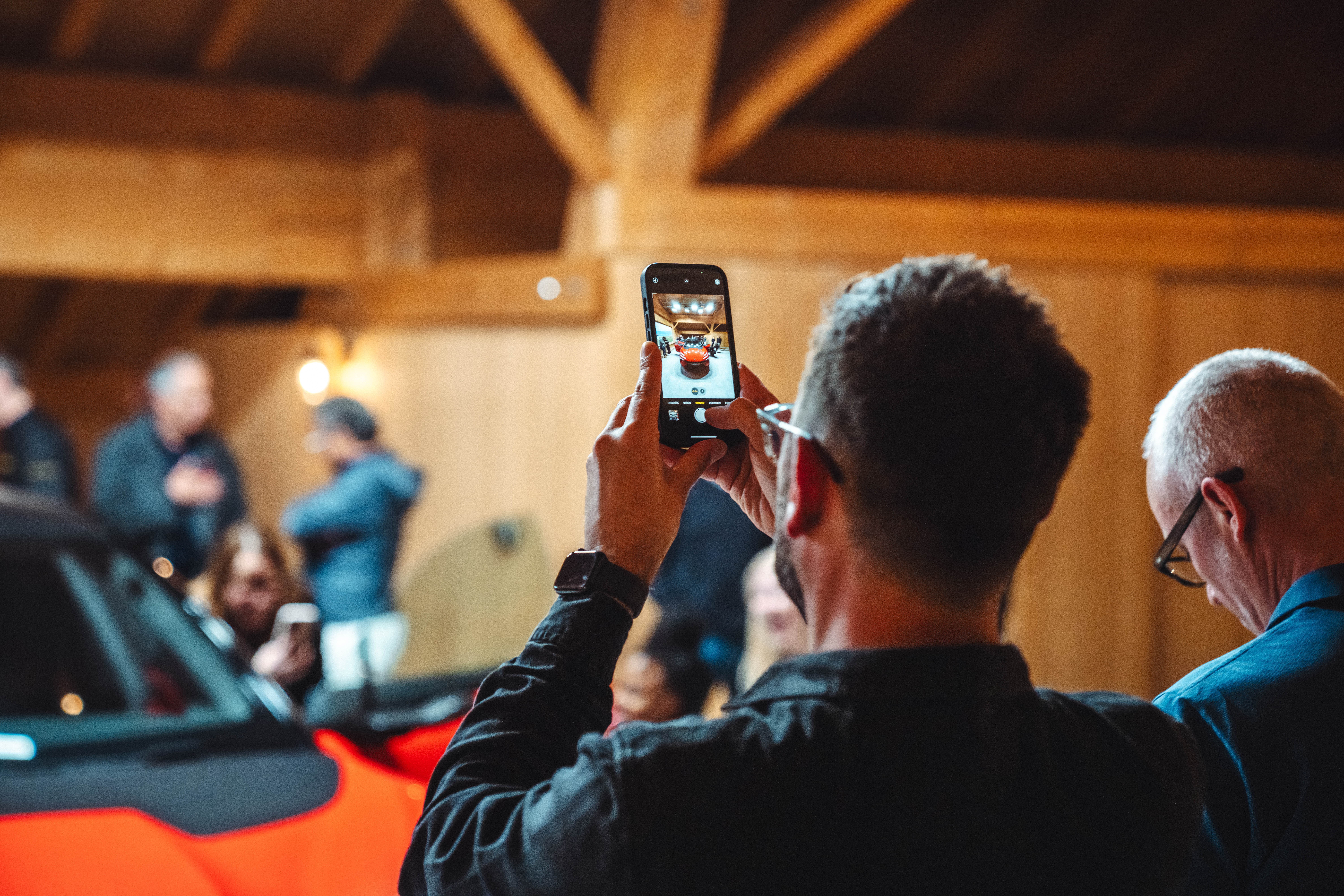 A man taking a phot of a red Lotus Emeya inside a stylish barn